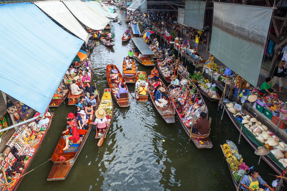 Barcos cheios de turistas e vendedores se alinham lado a lado no canal do mercado flutuante Damnoen Saduak, com muitas frutas e lembranças à venda.