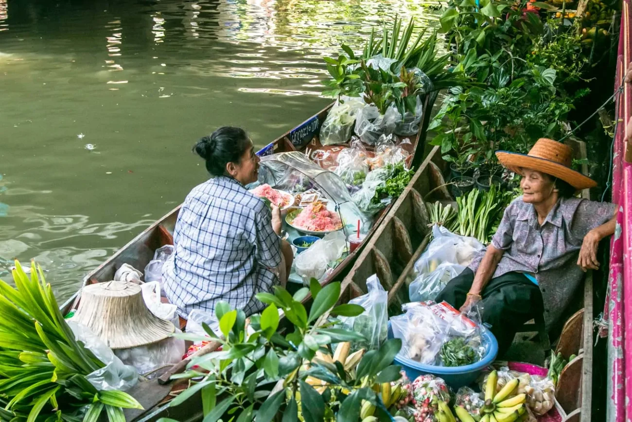 : Duas mulheres em barco vendem vegetais e plantas em canal tailandês.