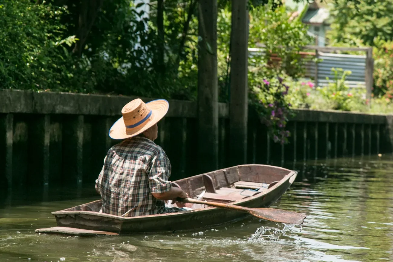 Pessoa rema sozinha em canal cercado de vegetação densa em um barco de madeira.