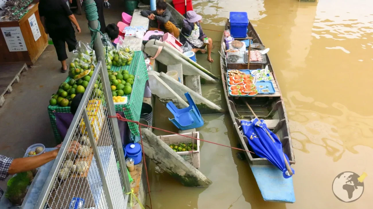 Cais de mercado flutuante em Bangkok com vendedores em barcos e frutas expostas à beira do canal.