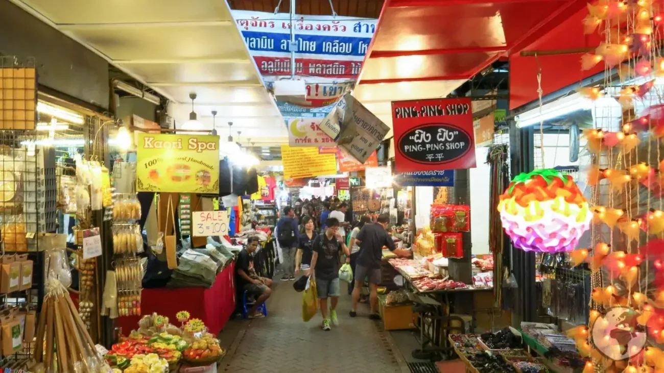 Corredor movimentado de um mercado coberto em Bangkok com lojas e letreiros coloridos dos dois lados.