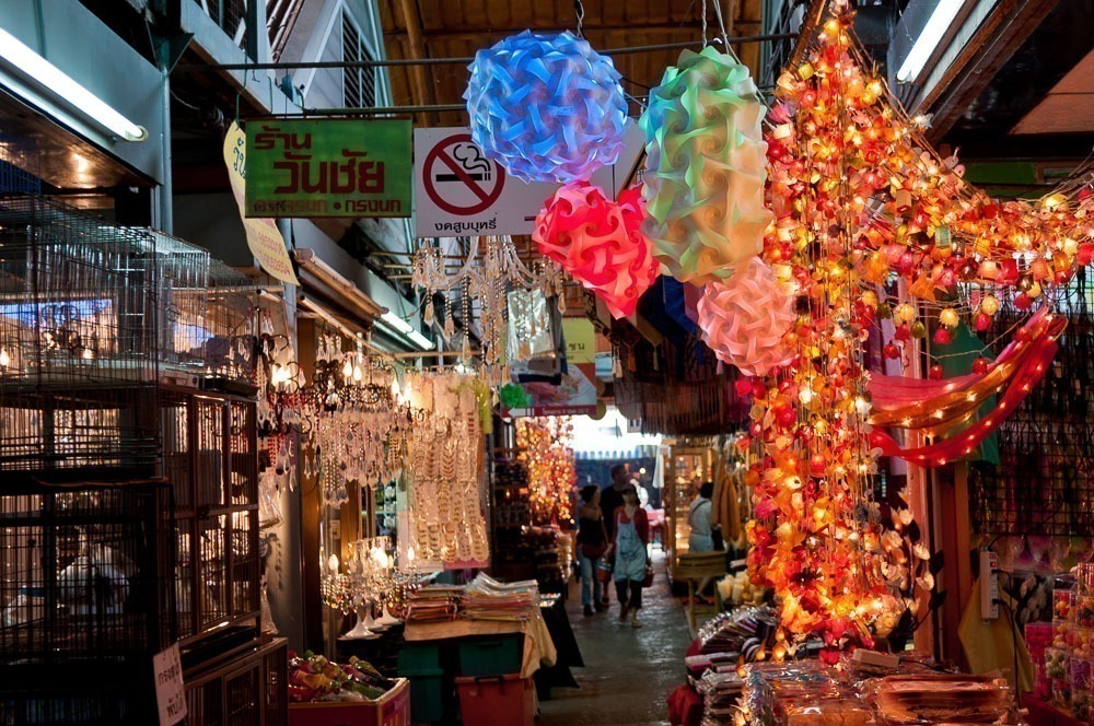 Luminárias artesanais e objetos decorativos iluminam um corredor movimentado do mercado de Chatuchak.