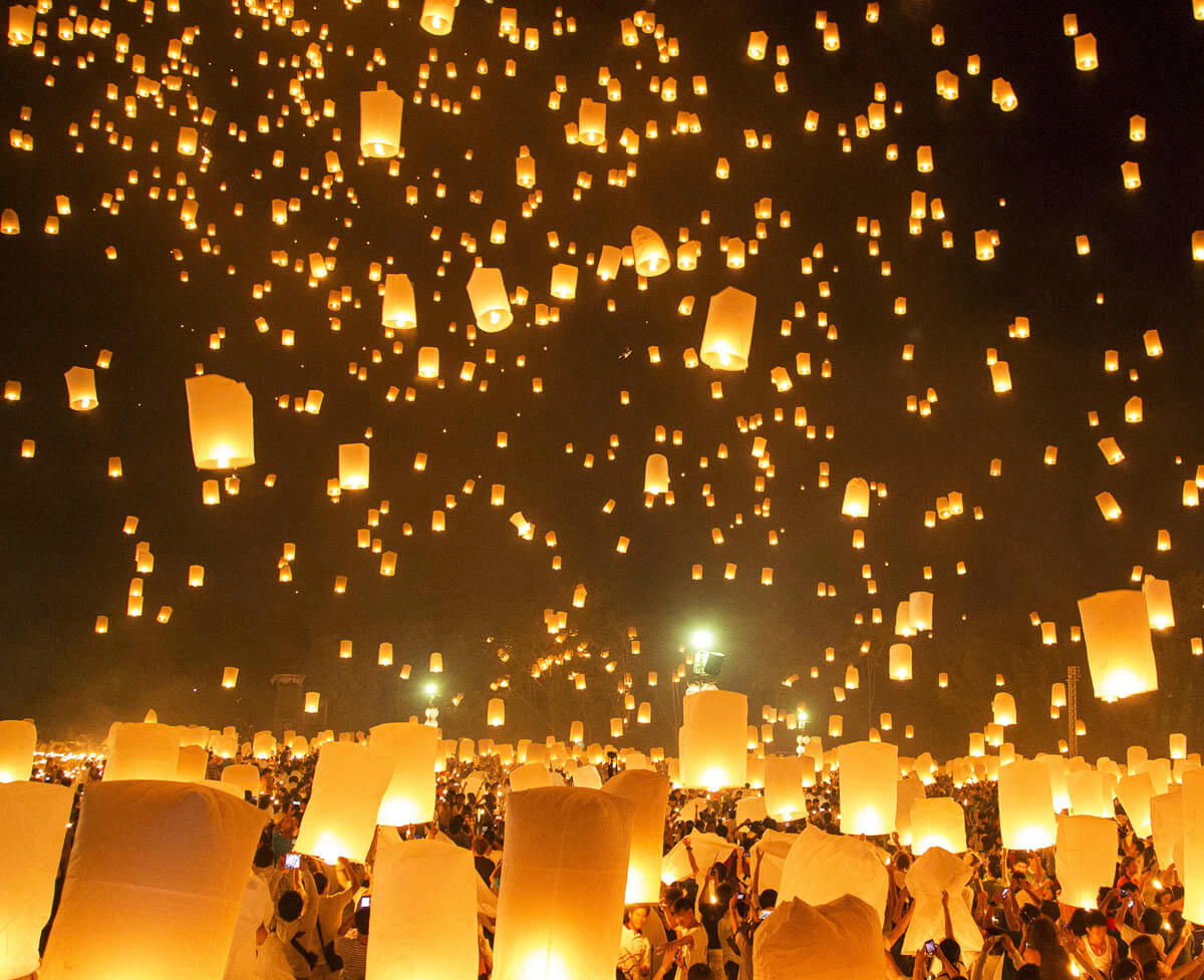 Centenas de lanternas iluminadas sendo soltas no céu noturno durante o festival Yi Peng em Chiang Mai.