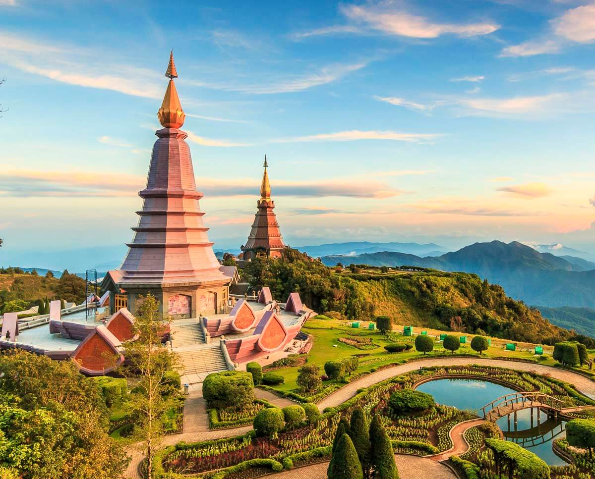 As duas estupas gêmeas do Parque Nacional Doi Inthanon em Chiang Mai ao entardecer, rodeadas por jardins floridos e montanhas ao fundo.