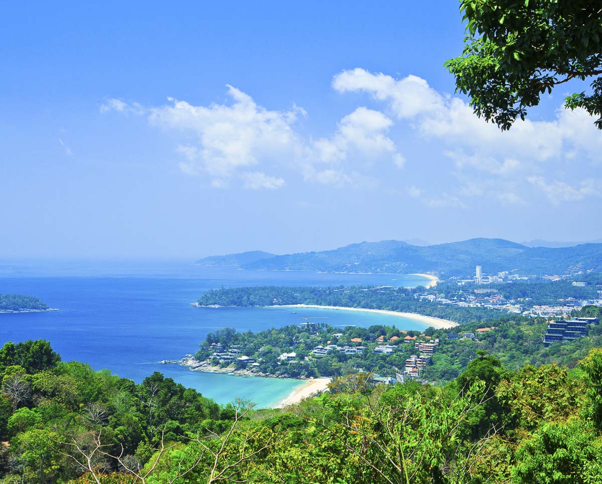 Vista panorâmica de Phuket a partir de um mirante, mostrando o mar azul, praias em formato de baía e a cidade entre colinas verdes.