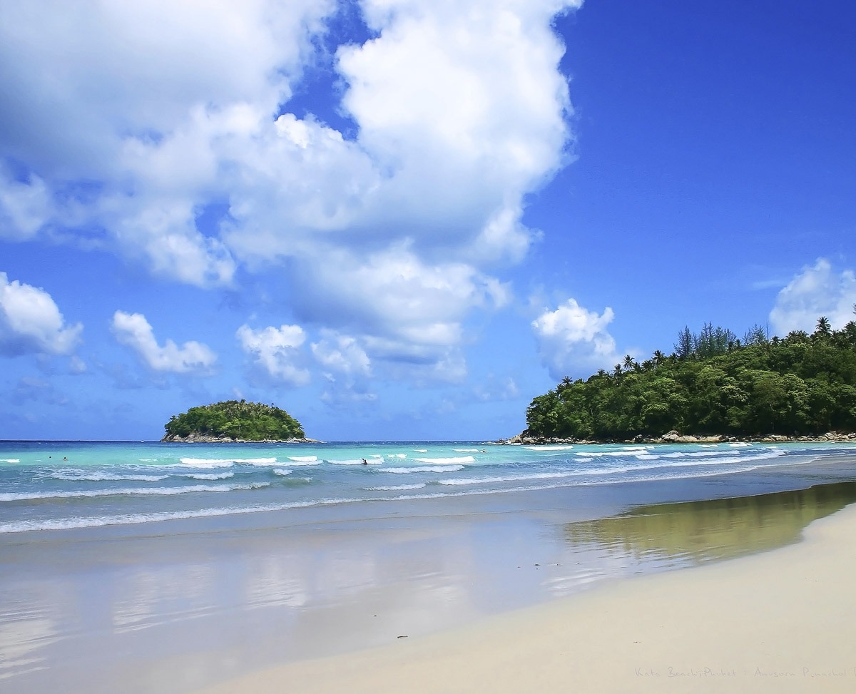 Praia com areia clara e mar azul esverdeado, com vegetação densa de um lado e uma pequena ilha no horizonte.