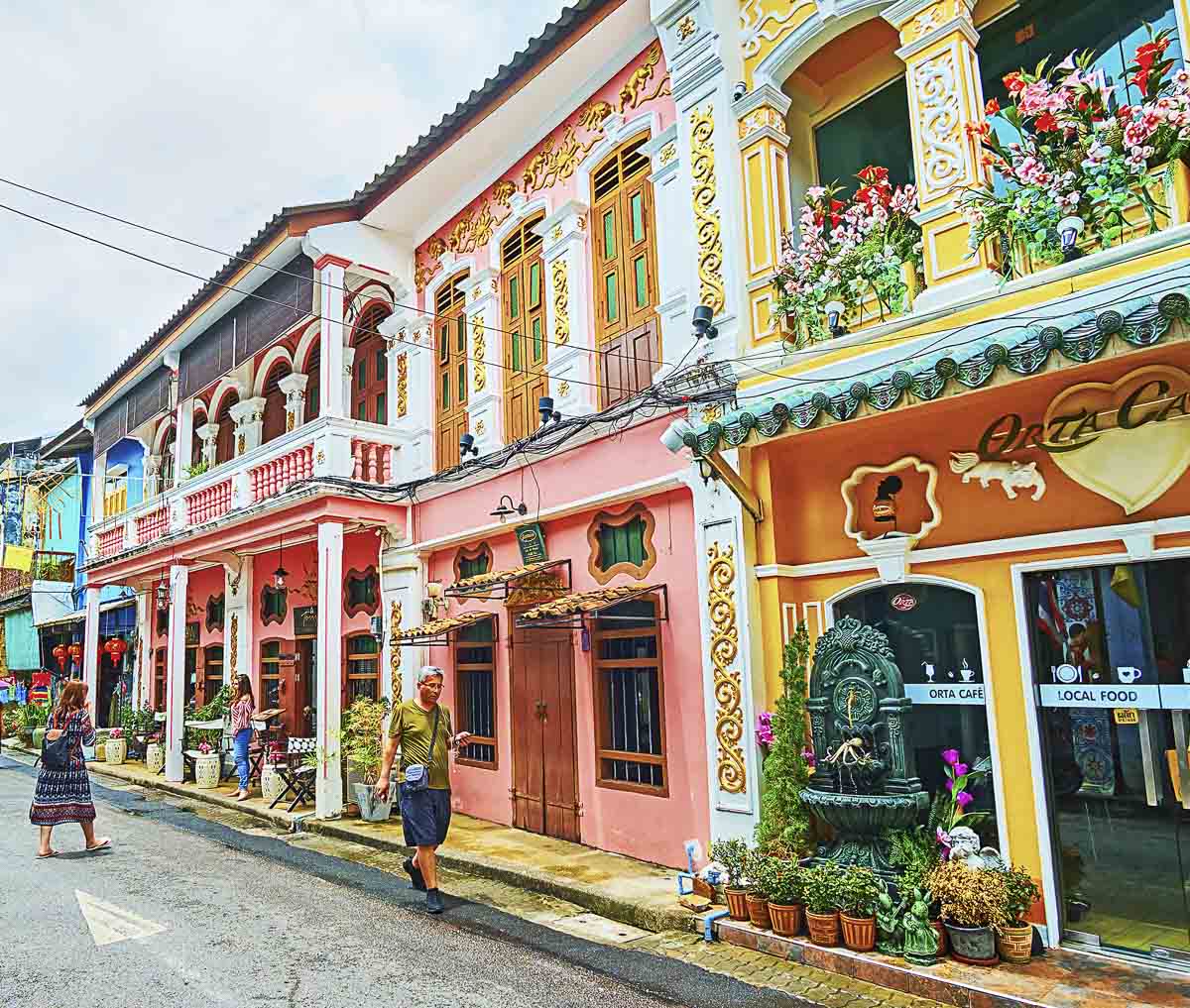 Fachadas coloridas e ornamentadas de casas coloniais no centro histórico de Phuket, com flores e pedestres.
