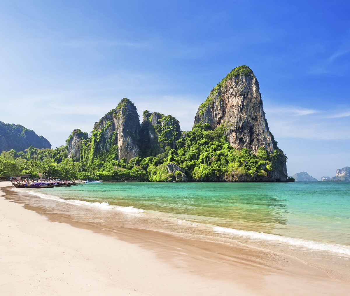 Praia de Railay em Krabi com areia clara, mar esverdeado e falésias cobertas por vegetação tropical.
