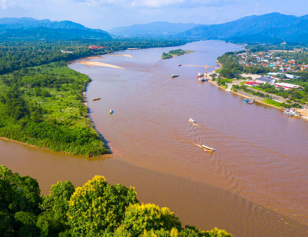 Vista aérea do Triângulo Dourado em Chiang Rai, com rios marrons se encontrando entre áreas verdes e pequenas cidades.