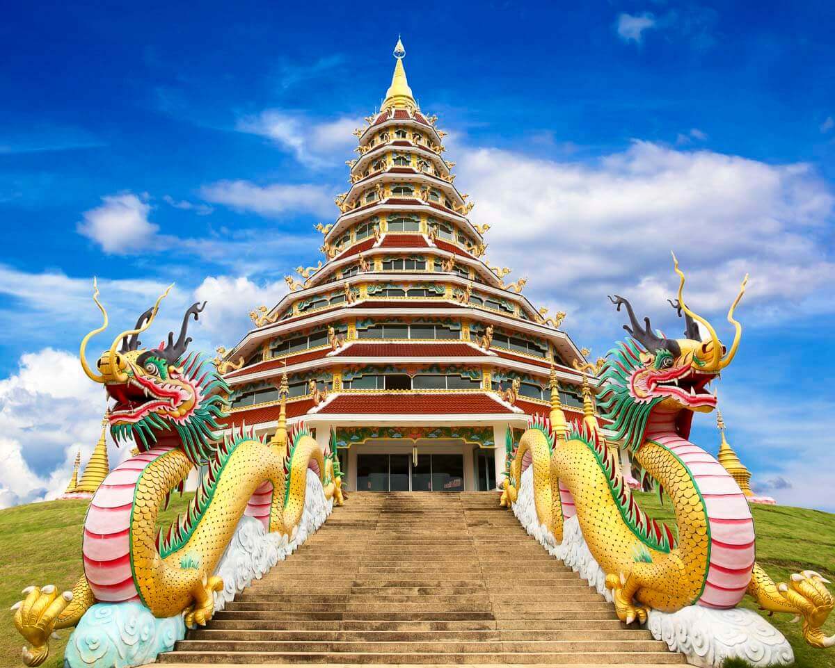 Grande templo branco em forma de pagode com escadaria ladeada por dragões dourados e céu azul ao fundo.
