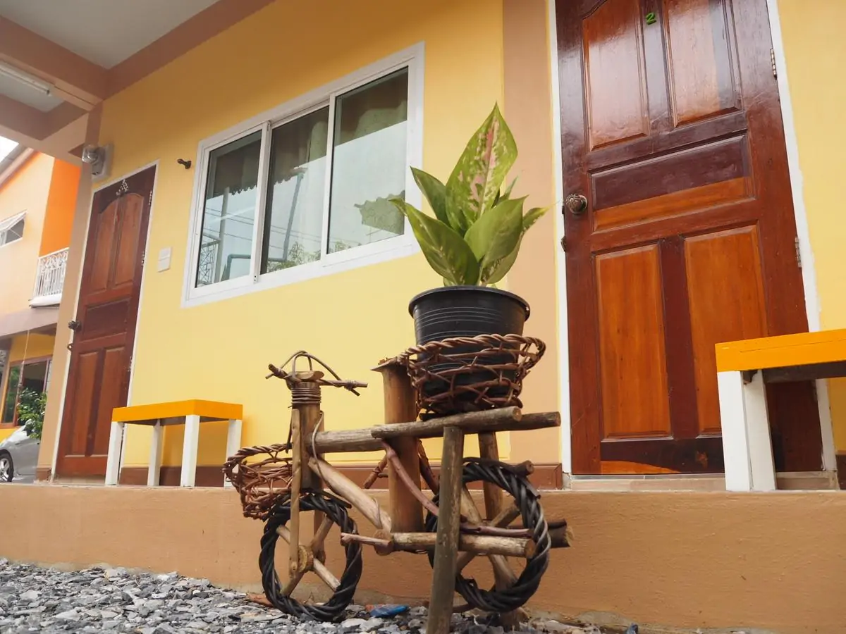 Entrada de pousada em Ayutthaya com paredes amarelas e decoração simples com vaso sobre bicicleta de madeira.