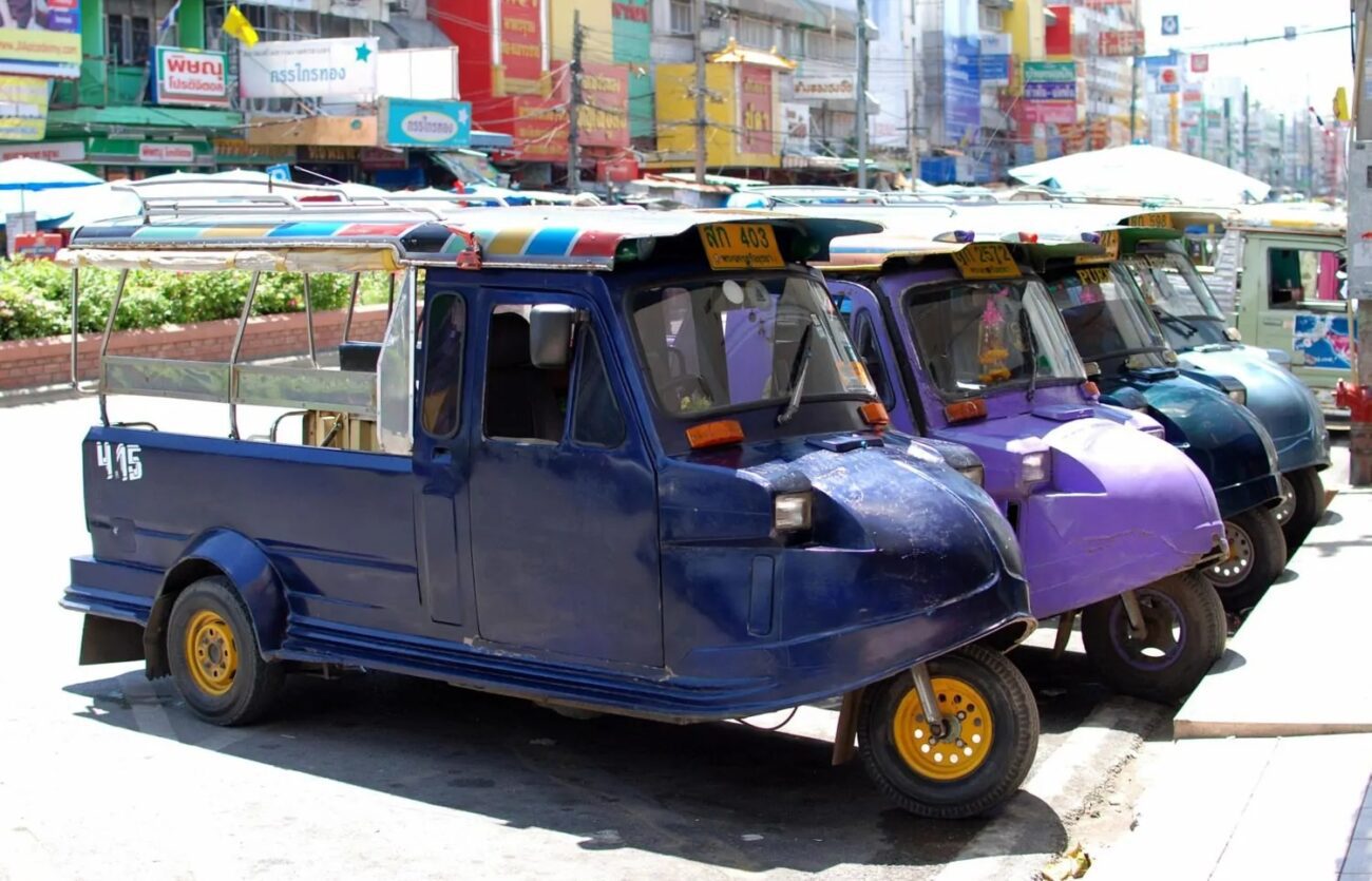 Tuk-tuks coloridos estacionados lado a lado em uma rua movimentada de Ayutthaya, Tailândia.