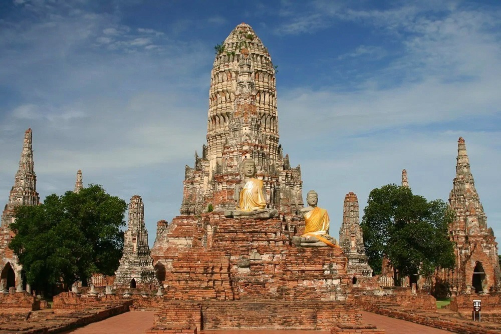 Templo de Wat Chaiwatthanaram em Ayutthaya com estátuas de Buda em destaque e céu azul ao fundo.