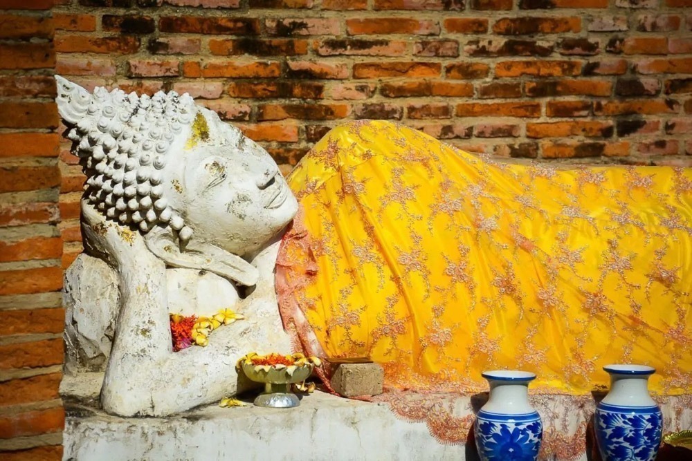Escultura de Buda deitado coberta por manto amarelo, ao lado de vasos azuis decorativos.