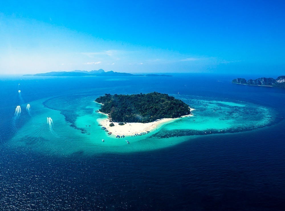 Ilha Bamboo vista de cima, cercada por águas cristalinas azul-turquesa e recifes de coral, com uma faixa de areia branca em contraste com a vegetação verde densa no centro.