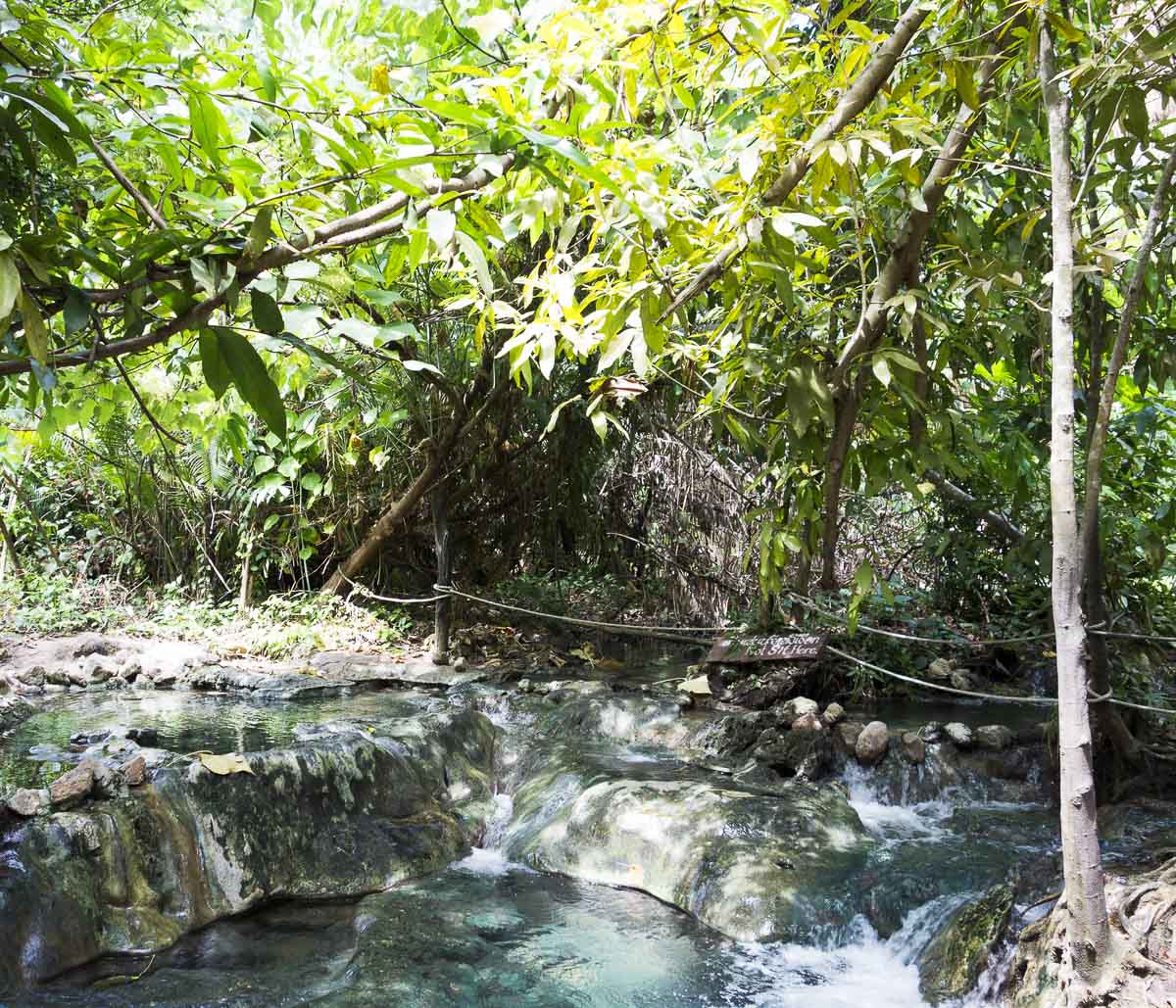 Piscinas naturais de águas termais cercadas por árvores e vegetação densa em Namtok Ron, Krabi.