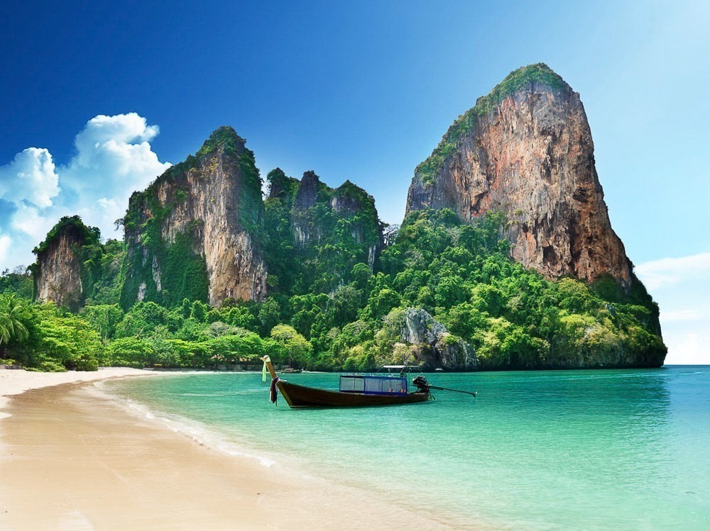 Praia de Railay com água azul-turquesa e falésias de calcário cobertas por vegetação exuberante ao fundo.