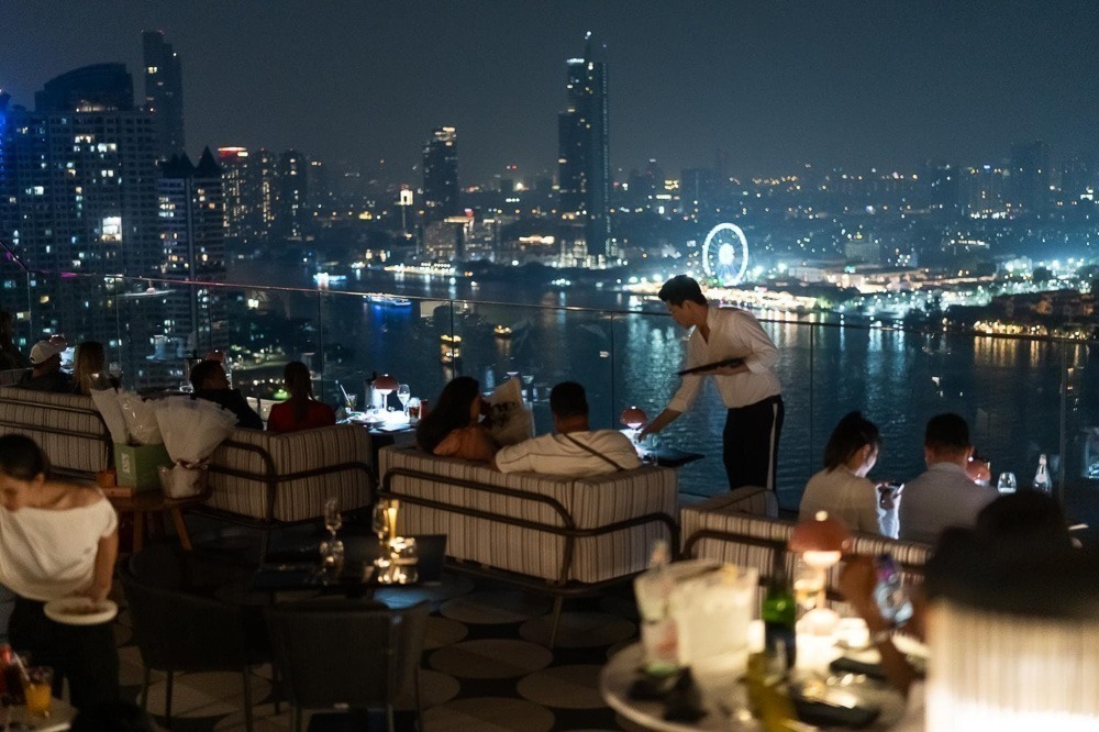 SEEN Restaurant & Bar com mesas ao ar livre e vista noturna do rio Chao Phraya e roda-gigante iluminada.