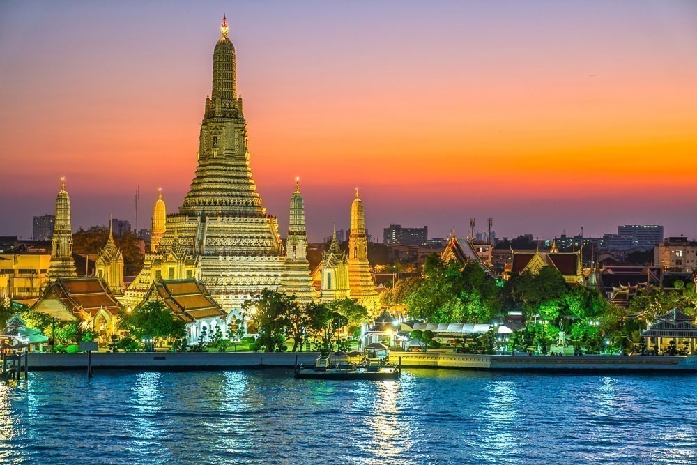 Templo Wat Arun iluminado ao entardecer, refletido no rio Chao Phraya.