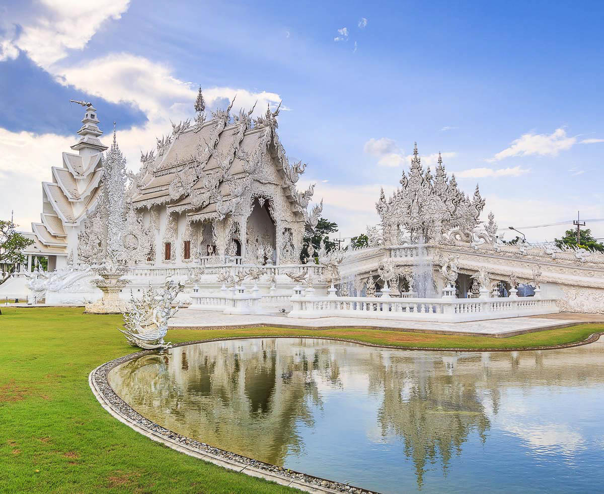 Wat Rong Khun, o templo branco em Chiang Rai, com sua fachada esculpida em detalhes e refletida no espelho d’água à frente.