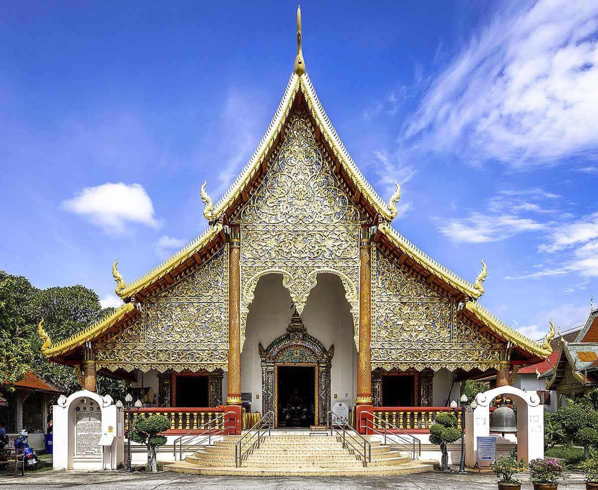 Fachada principal do Wat Chiang Man em Chiang Mai, com ornamentos dourados e céu azul ao fundo.