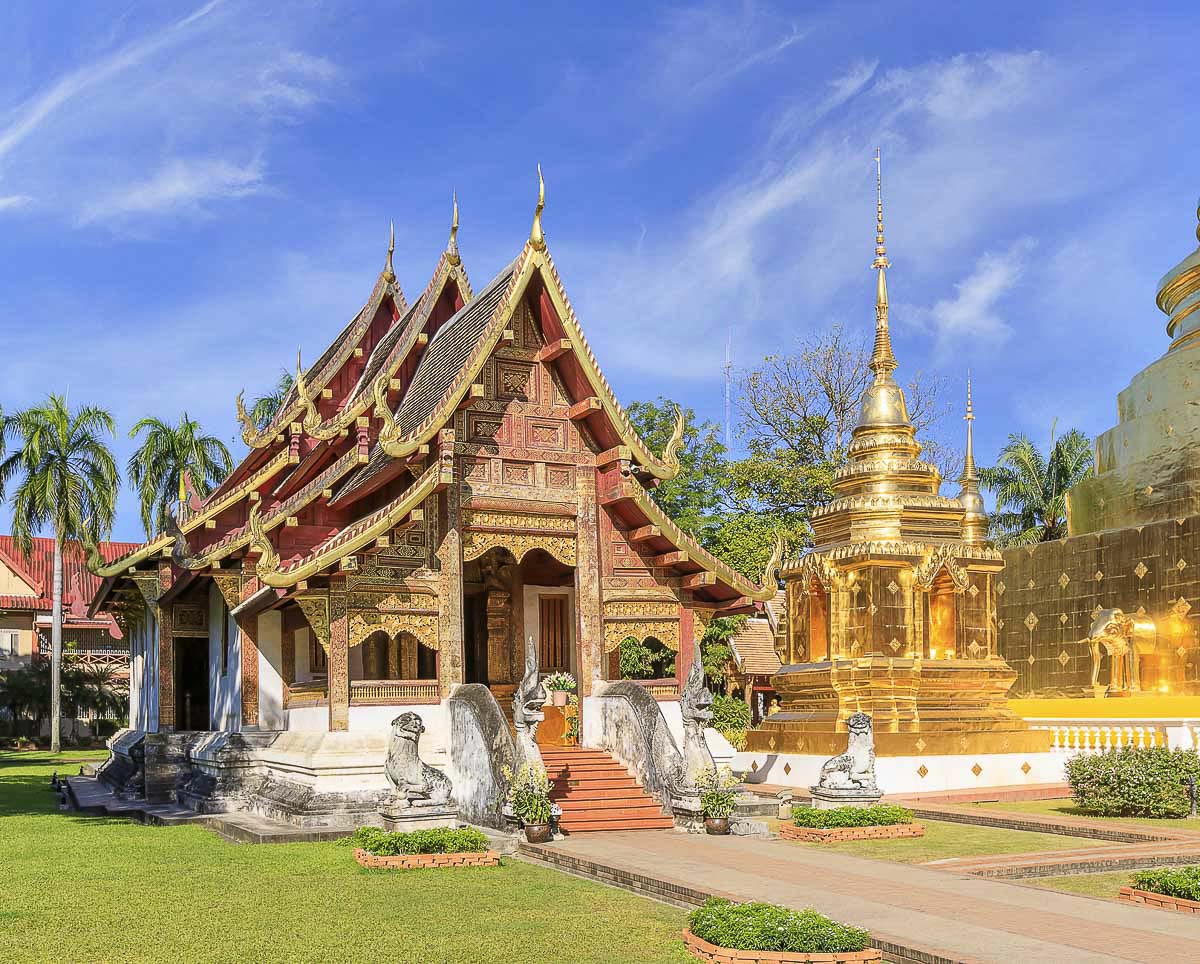 Templo Wat Phra Singh com detalhes dourados e telhado tradicional, ao lado de um pequeno chedi dourado em Chiang Mai, Tailândia.