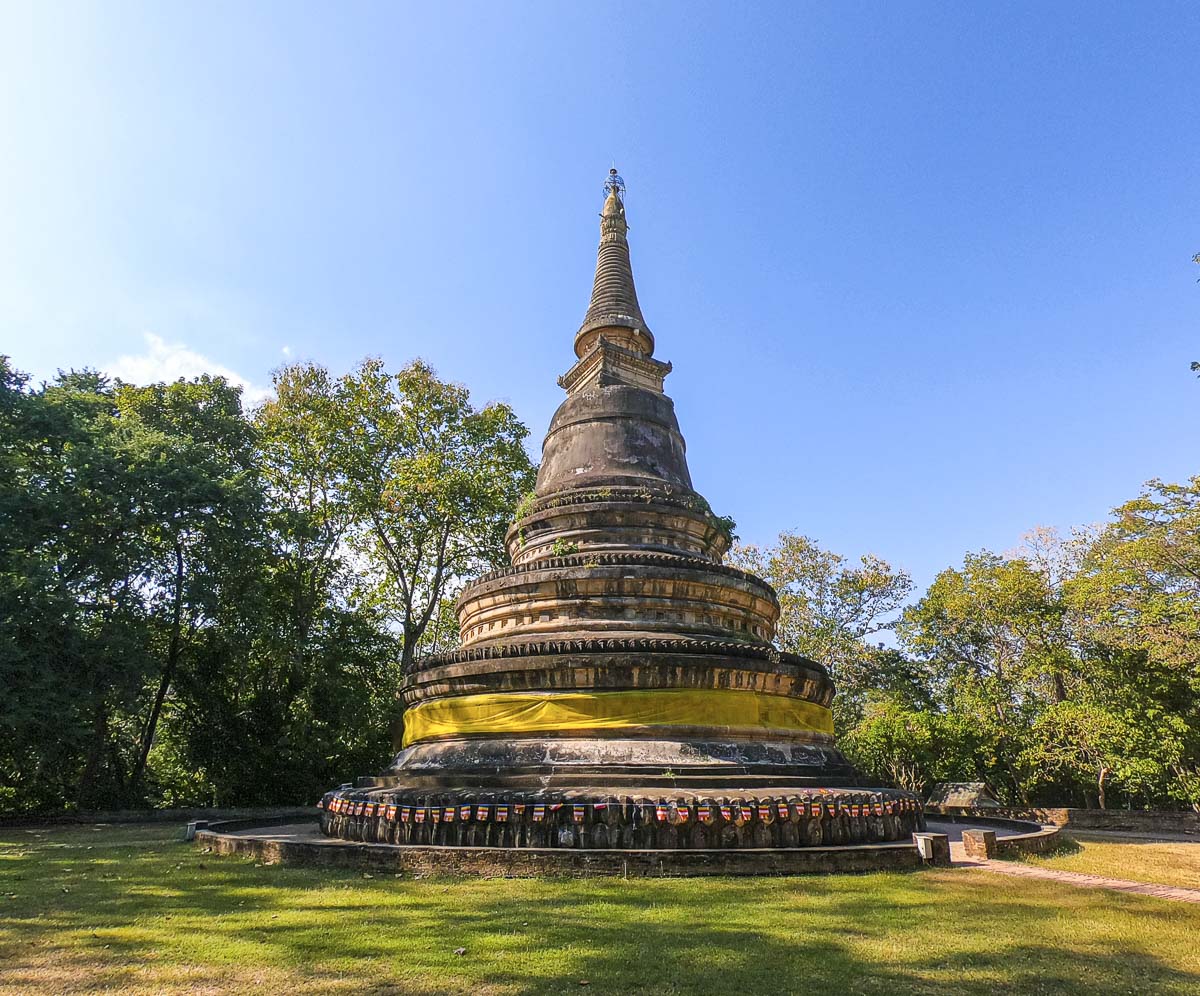 Estupa antiga de pedra coberta por musgo e vegetação ao redor no templo Wat Umong, em Chiang Mai.