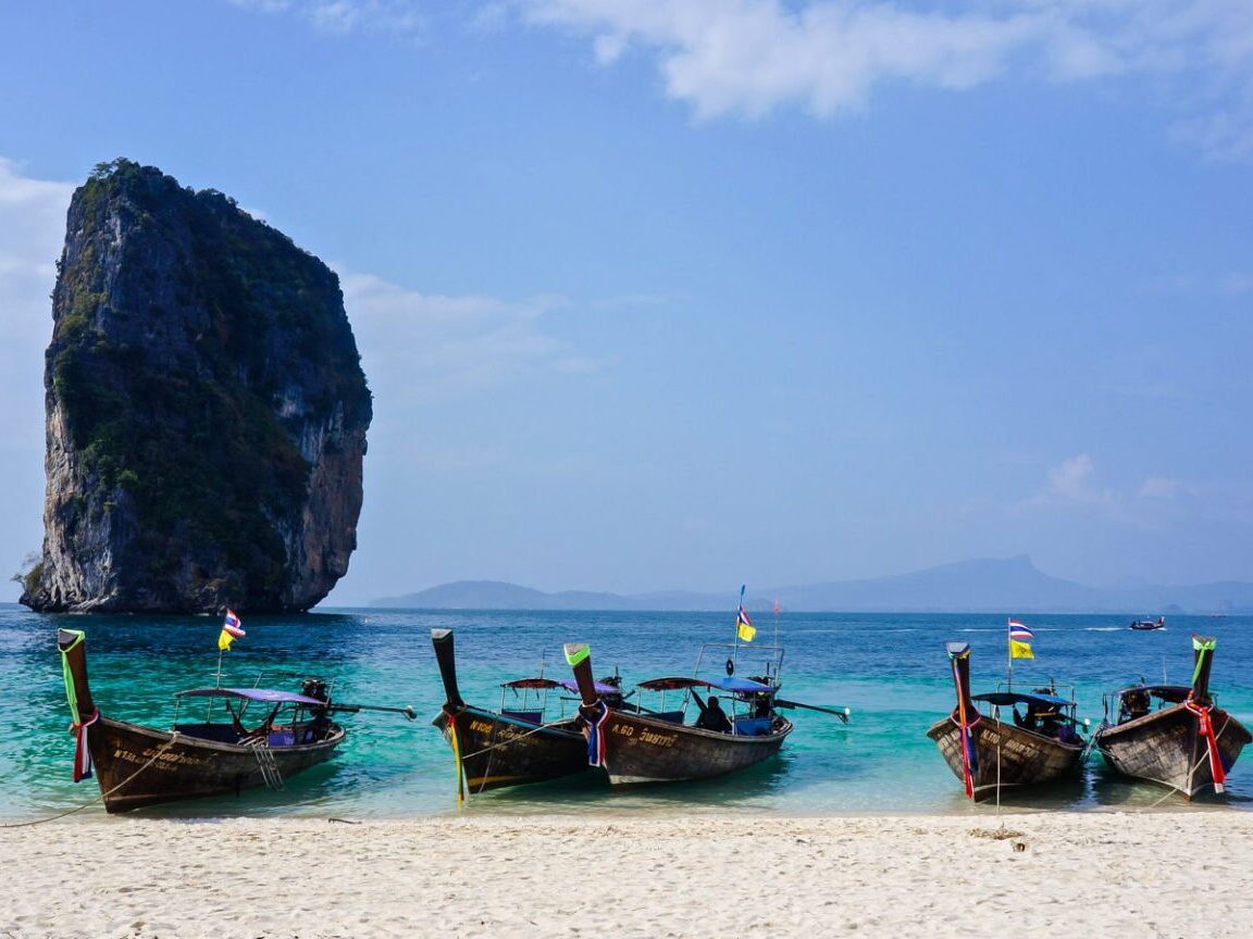 Praia em Krabi, com formação rochosa e quatro barcos tradicionais.