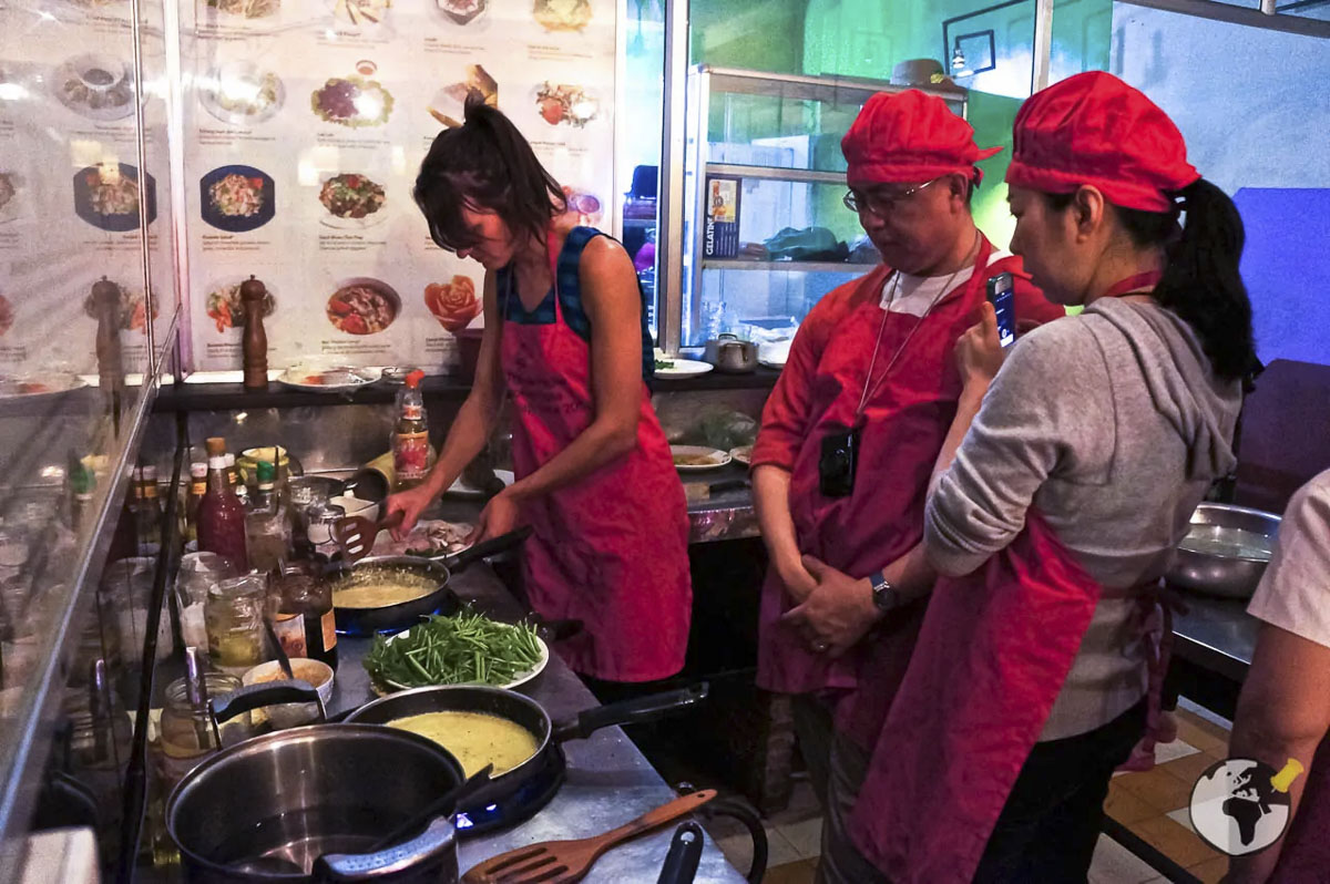 Pessoas em aula de culinária tailandesa preparando pratos típicos em uma cozinha.