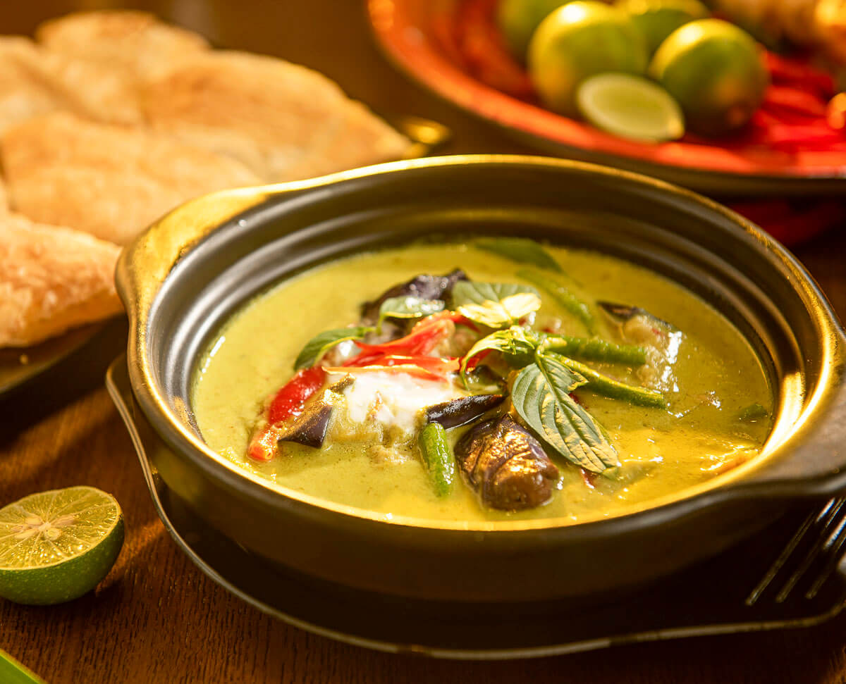 Tigela com curry verde tailandês servido com vegetais e manjericão.