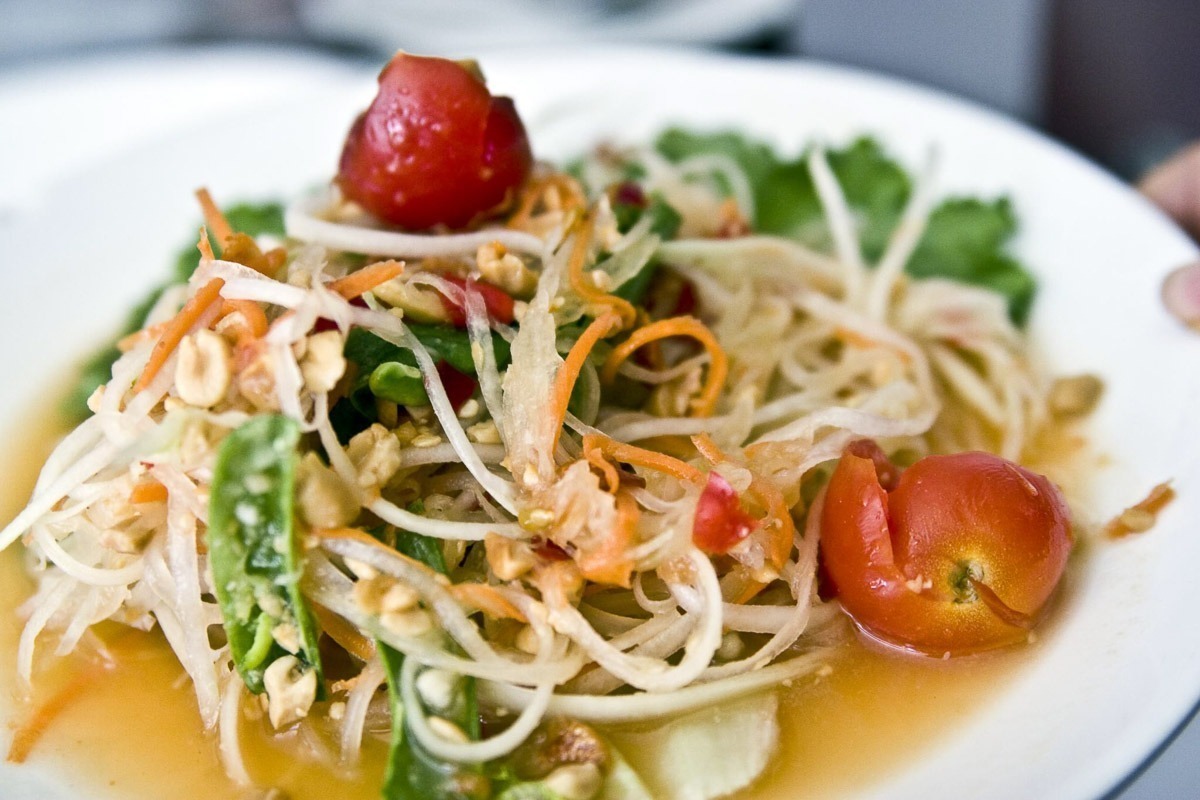 Salada de mamão verde com tomate, amendoim e vegetais servida em prato branco.