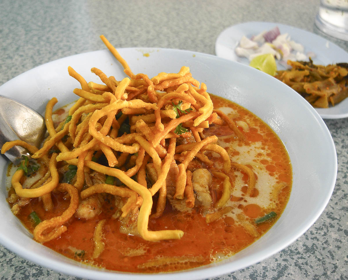 Tigela de khao soi com caldo de curry vermelho e macarrão frito por cima.
