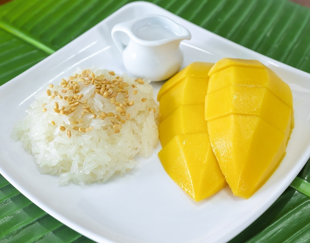 Manga fatiada servida com arroz glutinoso coberto com sementes de gergelim e leite de coco.