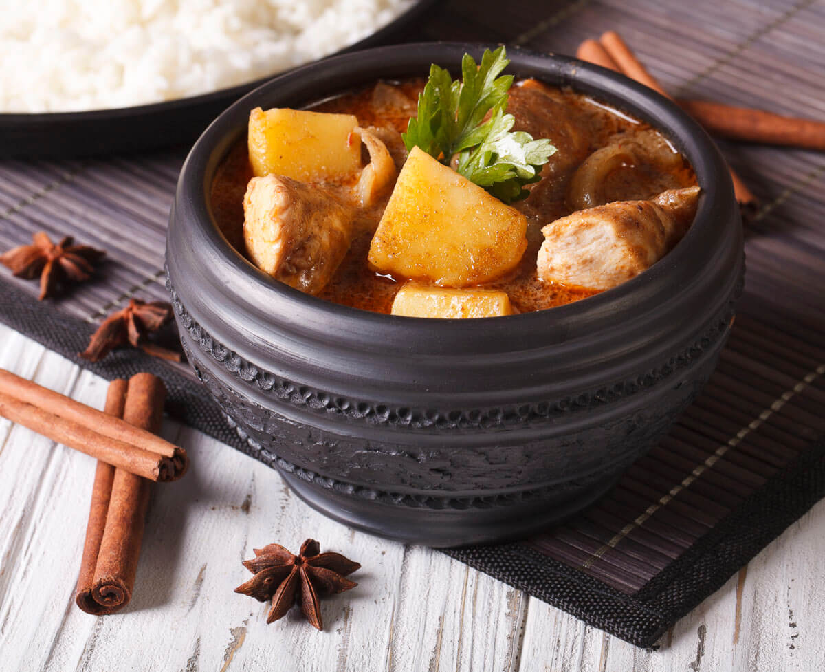 Curry tailandês Massaman com frango, batata e temperos em tigela preta.