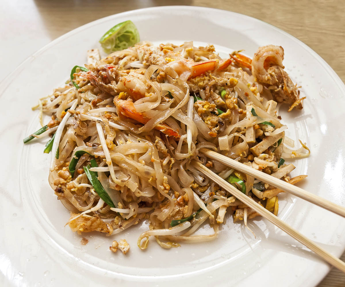 Pad Thai com camarões, broto de feijão e limão servido com hashis.