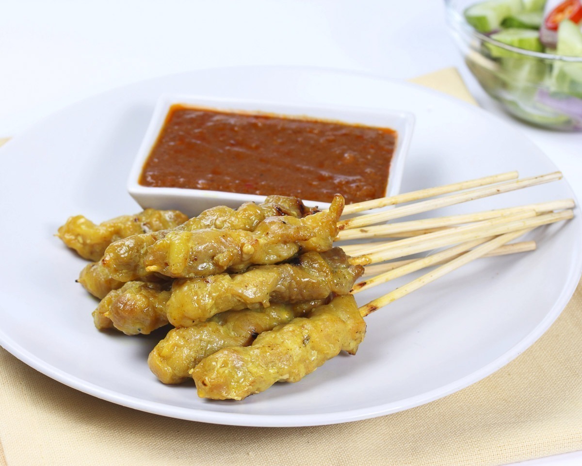Espetinhos de carne satay com molho de amendoim em prato branco.