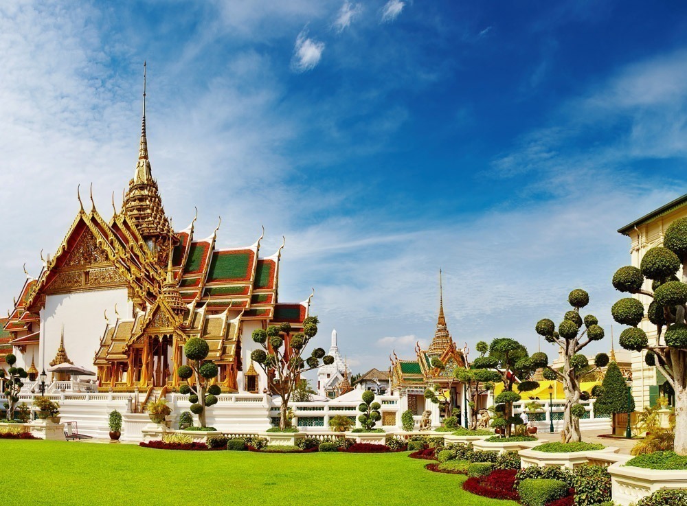 Templo ricamente decorado no complexo do Grande Palácio de Bangkok, rodeado por jardins bem cuidados.