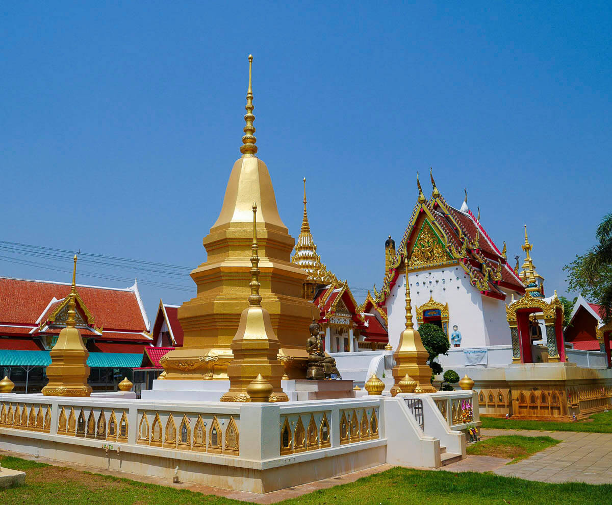 Templo tailandês com diversas estupas douradas e prédios ornamentados em Kanchanaburi.