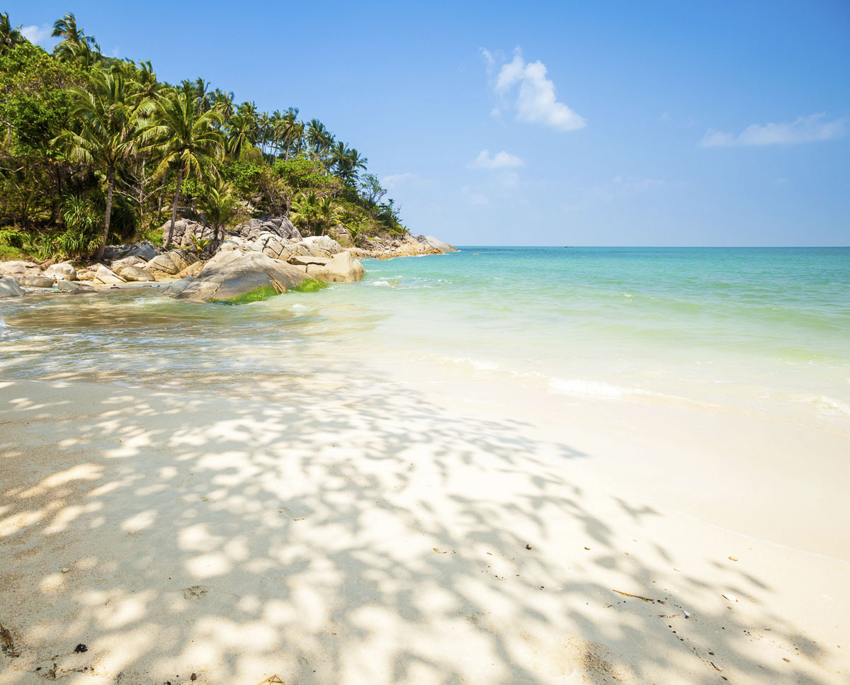 Praia paradisíaca com areia branca, sombra de coqueiros e mar em tons de verde e azul em Koh Phangan.