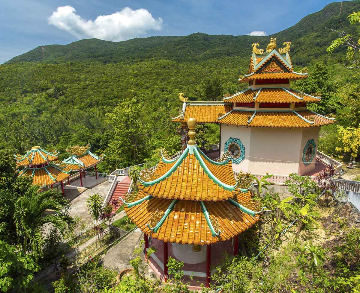 Templo budista com telhados laranja em estilo oriental rodeado por mata tropical e montanhas em Koh Phangan.