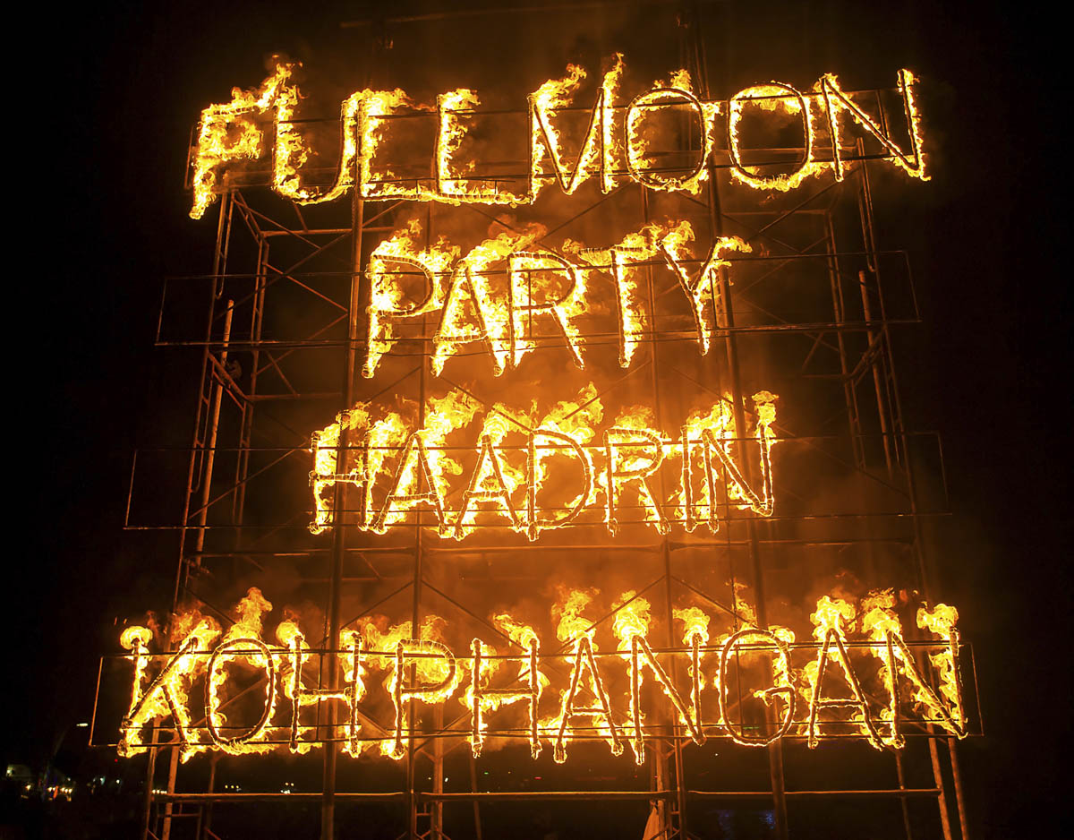 Letreiro em chamas com as palavras “FULL MOON PARTY HAAD RIN KOH PHANGAN” durante a noite.