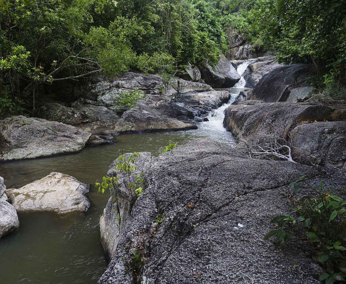 Cachoeira caindo entre rochas cercadas por floresta em Koh Phangan.