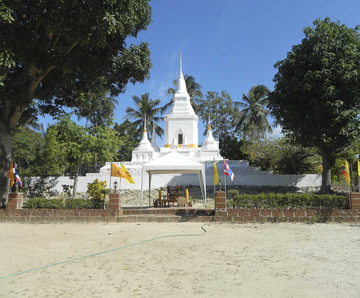 Chedi branco rodeado por árvores, com bandeiras tailandesas e espaço para cerimônias religiosas em Koh Phangan.