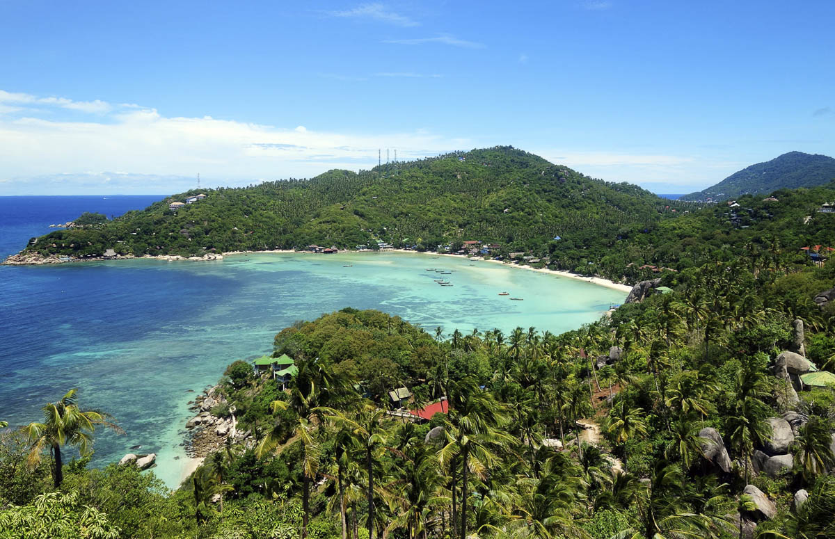 Baía de Koh Tao com mar em tons de azul e verde, cercada por colinas cobertas de vegetação tropical.