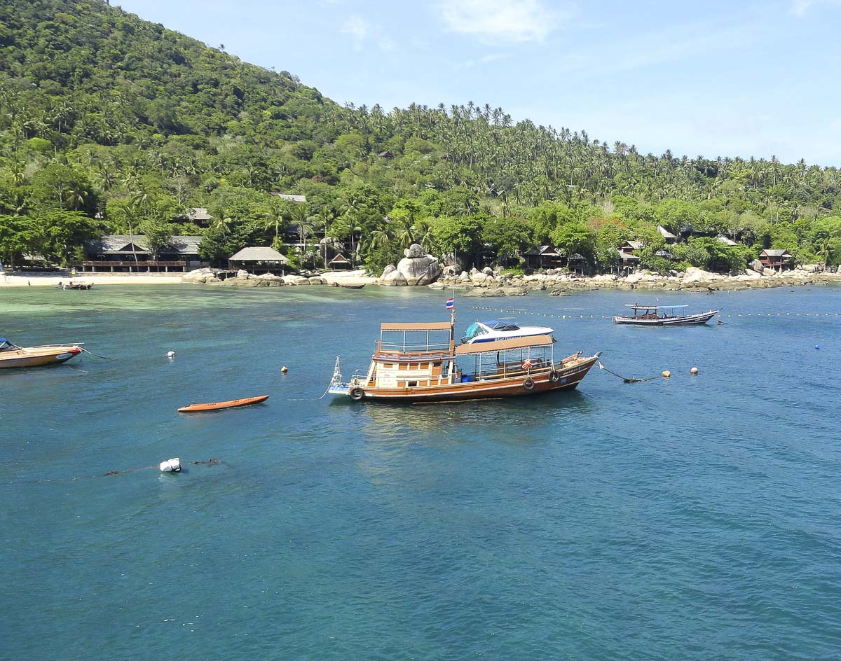 Barco de madeira tailandês flutuando em mar azul profundo próximo à costa de Koh Tao.