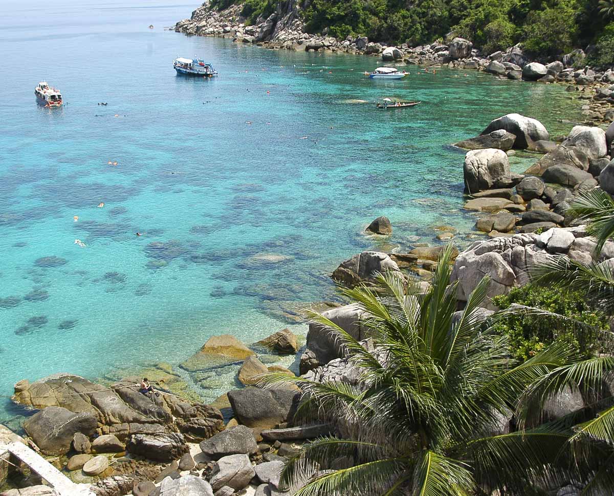 Baía com águas transparentes, grandes pedras e banhistas em Koh Tao.