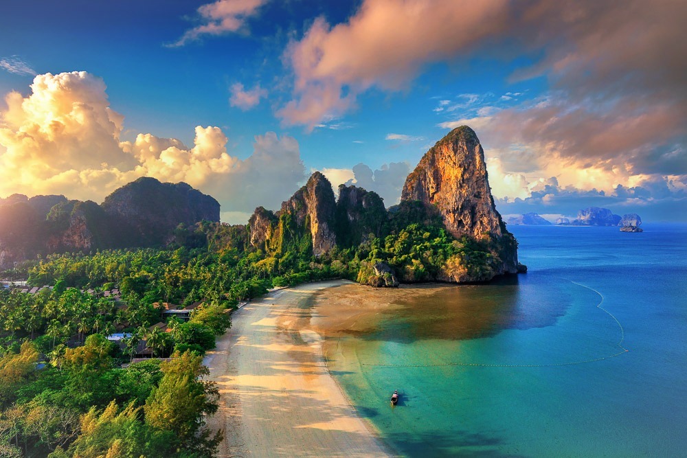 Vista aérea de Railay West mostrando praia curva, mar turquesa e falésias imponentes rodeadas por vegetação densa.