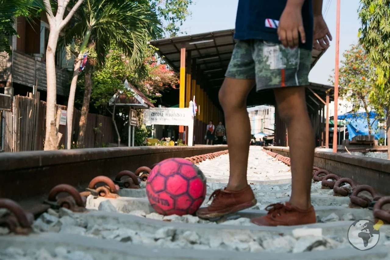 Criança com bola de futebol nos trilhos próximos à estação ferroviária de Maeklong.