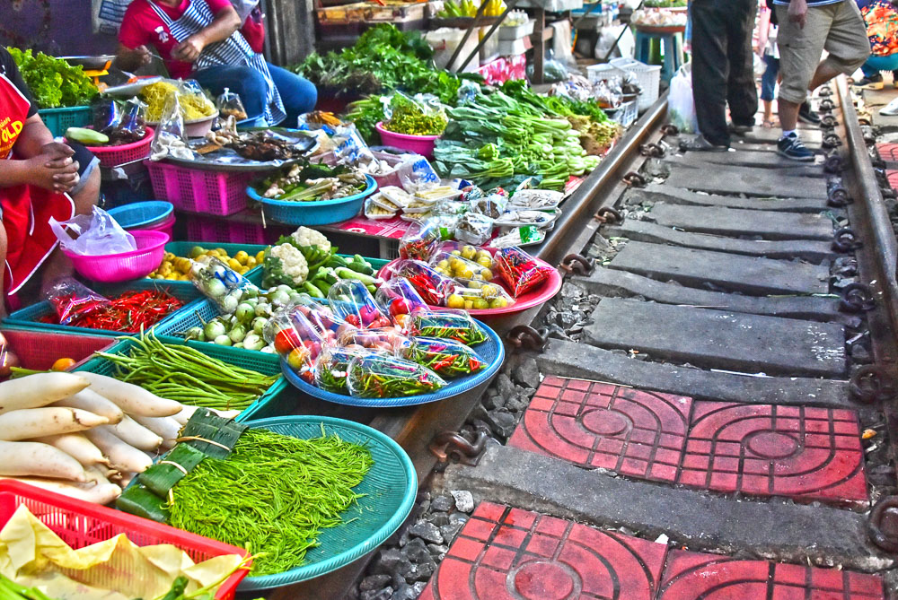 Cestos coloridos repletos de legumes e hortaliças organizados ao lado dos trilhos no mercado Maeklong.