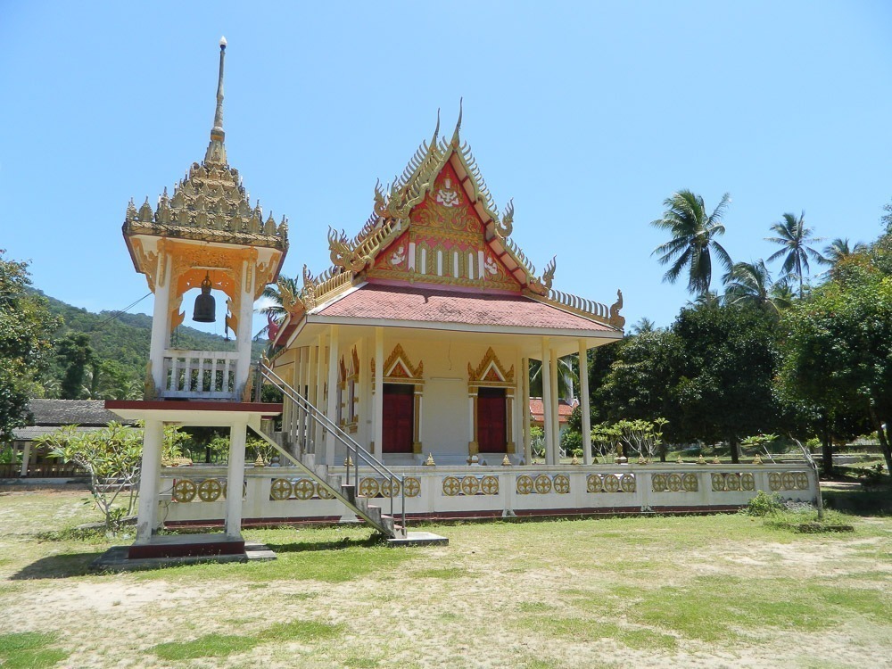 Templo tailandês colorido com sinos, escadas e telhado ornamentado em meio à natureza de Koh Phangan.